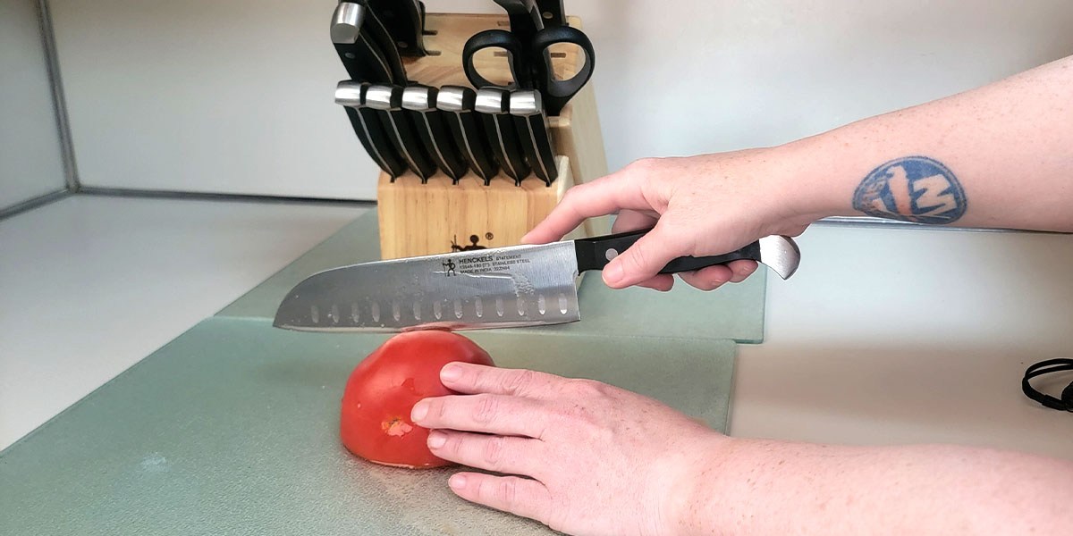 Person using kitchen knife to slice tomato