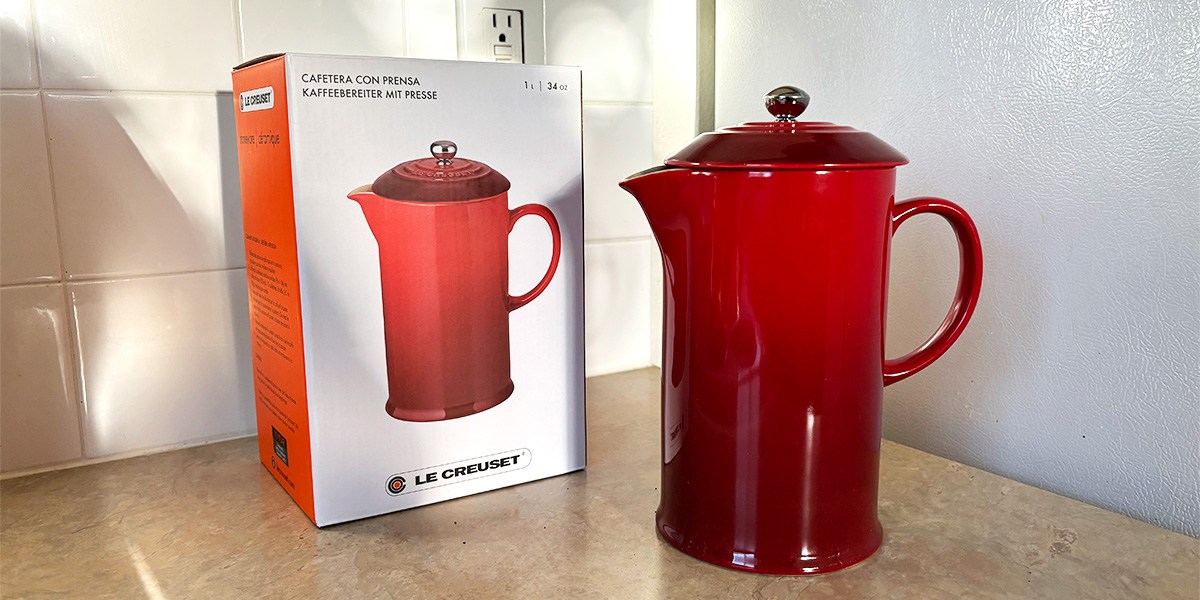 Red Le Creuset French Press on countertop next to product packaging