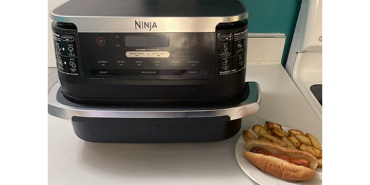 Ninja Foodi FlexBasket Air Fryer next to plate with hot dog and fries with partially open basket  Ninja Foodi FlexBasket Air Fryer next to plate with hot dog and fries with partially open basket