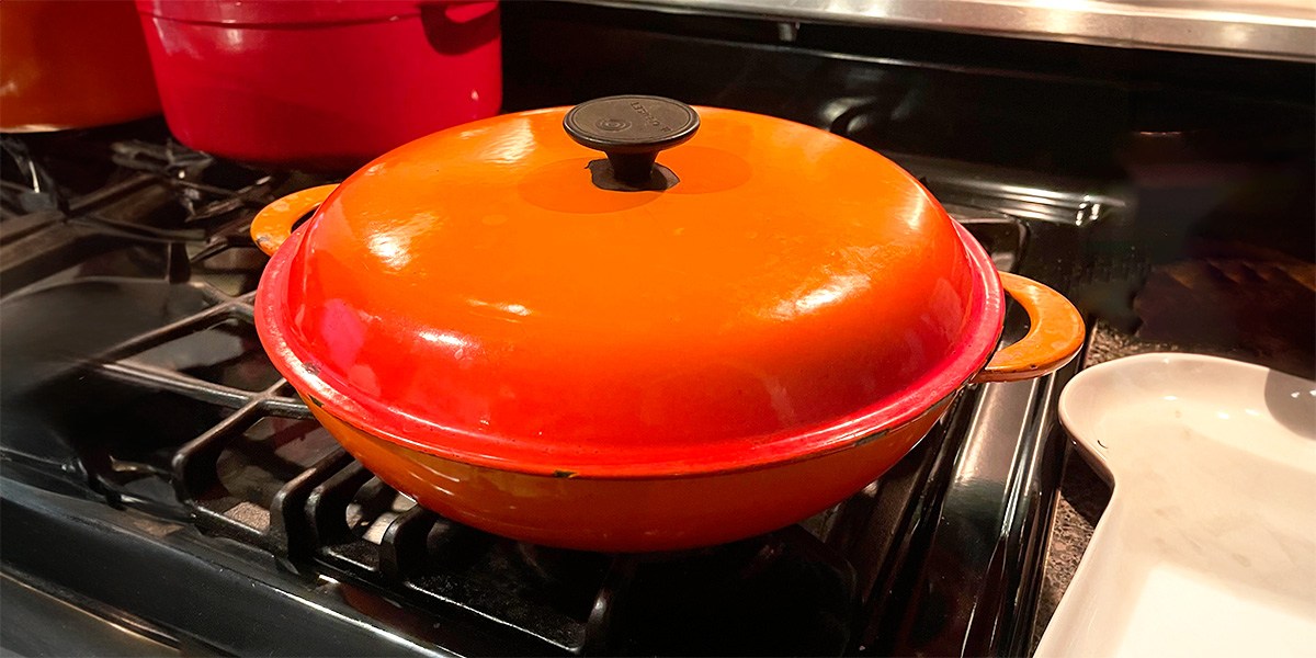 Orange Le Creuset Round Dutch Oven with lid on stove burner Orange Le Creuset Round Dutch Oven with lid on stove burner