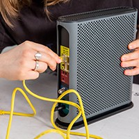 Person plugging in ethernet cable to ethernet port on modem-router