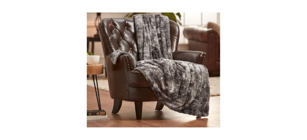 Chanasya Super Soft Fuzzy Faux Fur Throw Blanket in gray, lying on a brown leather chair