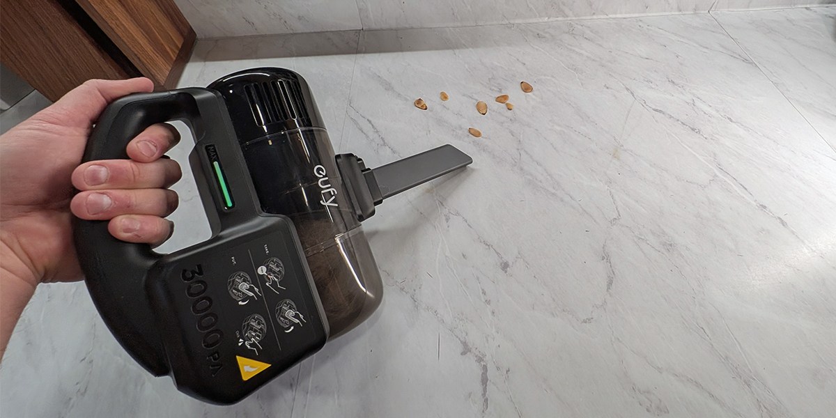 A person using a handheld cleaner to suck up almond's from a white stone countertop
