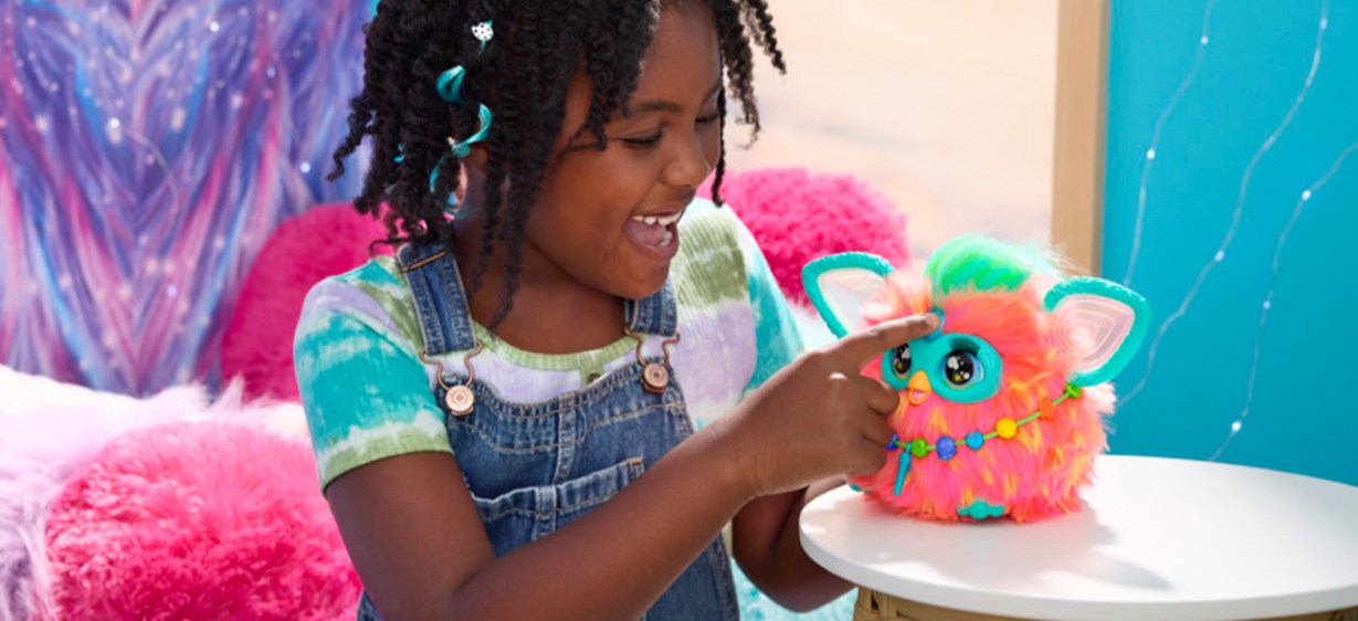 A child playing with a Furby toy that's sitting on a table